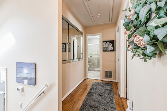 hall with light wood finished floors, visible vents, attic access, and baseboards