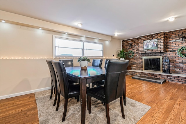 dining space with a brick fireplace, baseboards, and wood finished floors