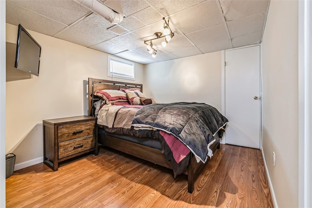 bedroom featuring light wood-style floors, baseboards, and a paneled ceiling