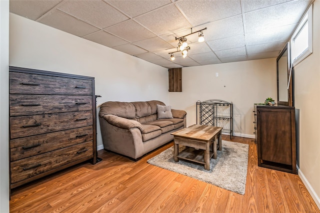 living room with light wood finished floors, a paneled ceiling, and baseboards