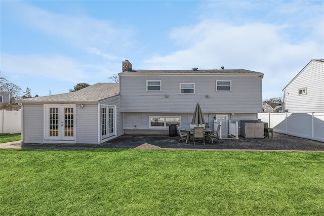 rear view of property with french doors, a yard, a fenced backyard, and a chimney