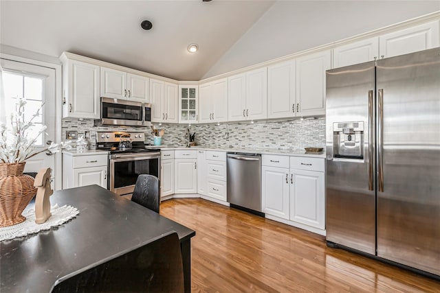 kitchen with stainless steel appliances, decorative backsplash, vaulted ceiling, white cabinets, and light wood-type flooring