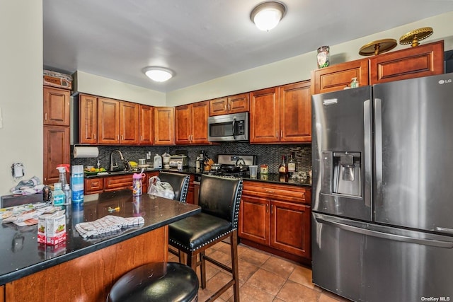 kitchen with decorative backsplash, appliances with stainless steel finishes, a kitchen breakfast bar, light tile patterned floors, and dark stone counters