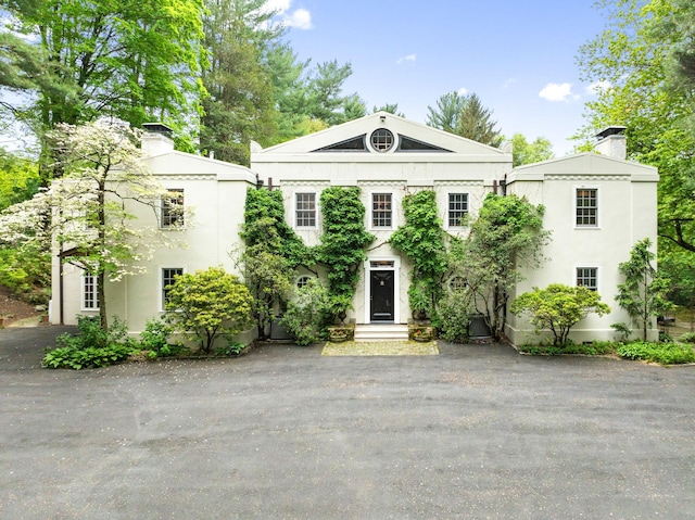 greek revival inspired property with a chimney and stucco siding