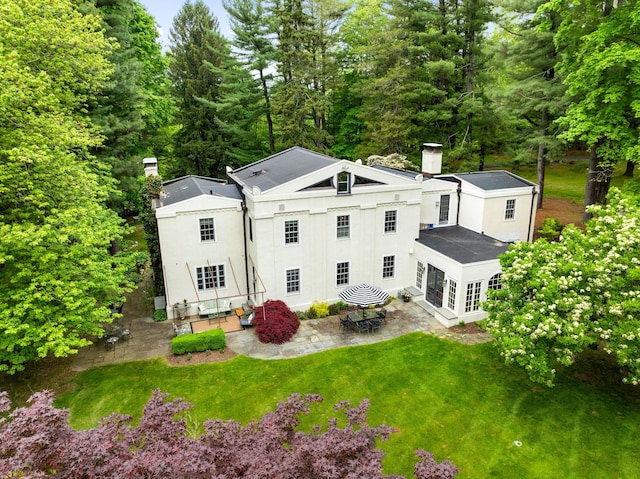 back of property with a chimney, a patio, a yard, and stucco siding