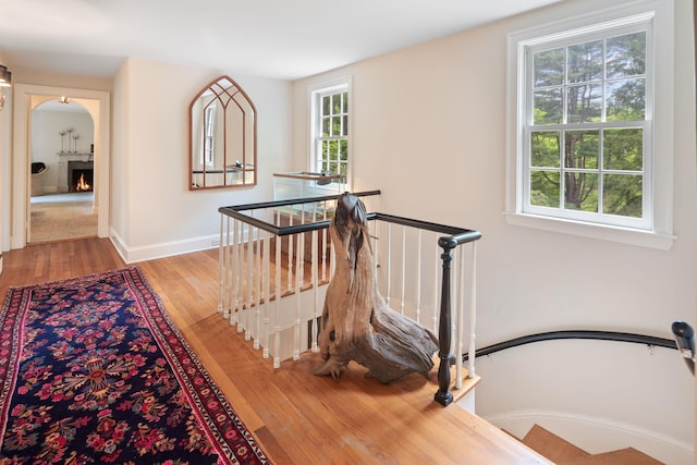 corridor featuring an upstairs landing, wood finished floors, baseboards, and arched walkways