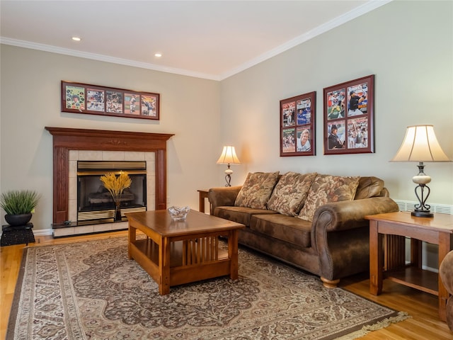 living room featuring a tiled fireplace, hardwood / wood-style floors, and crown molding