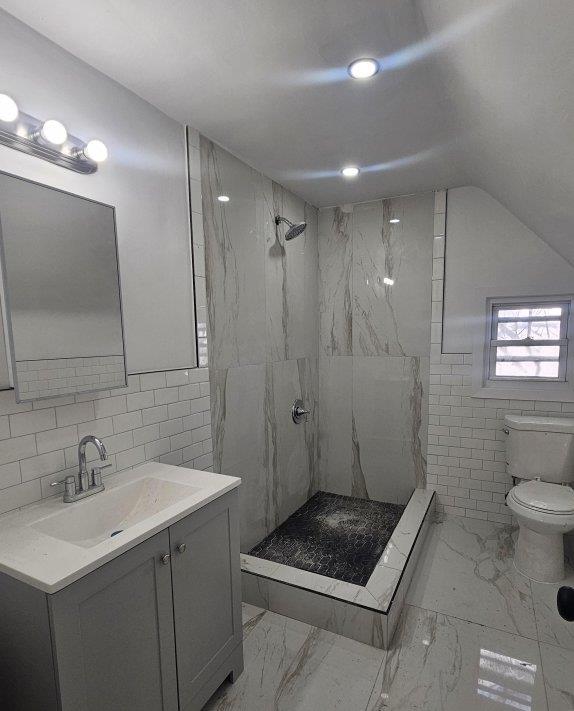 bathroom with vanity, toilet, a tile shower, and tile walls