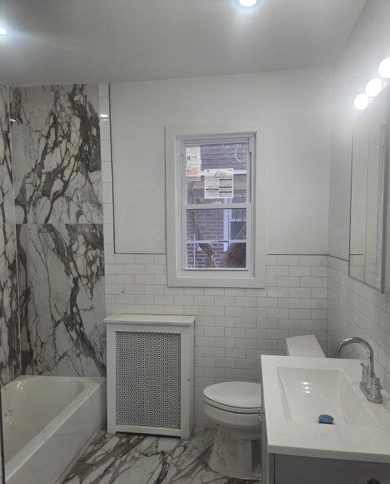 bathroom featuring toilet, a bathing tub, tile walls, radiator, and vanity