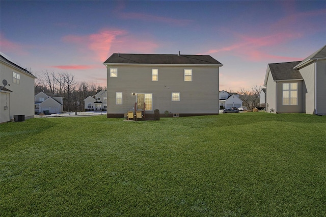 back house at dusk featuring central AC unit and a yard