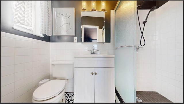 bathroom with tile walls, tiled shower, vanity, and toilet