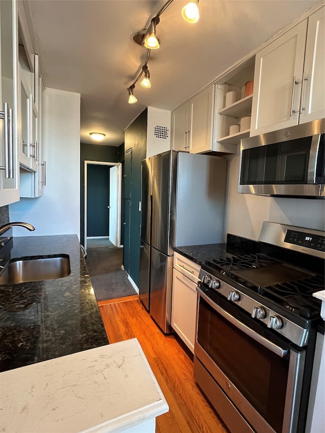 kitchen featuring white cabinets, appliances with stainless steel finishes, dark stone counters, light hardwood / wood-style floors, and sink