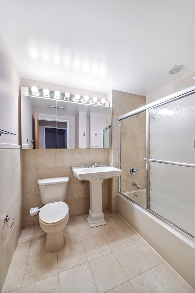 bathroom with tile patterned floors, bath / shower combo with glass door, toilet, and tile walls