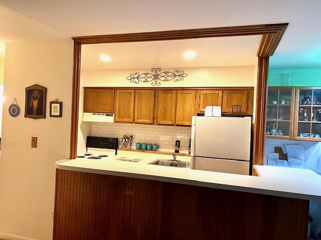 kitchen featuring tasteful backsplash, kitchen peninsula, white fridge, and range