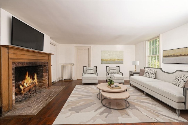 living room with radiator, dark wood-type flooring, and a brick fireplace