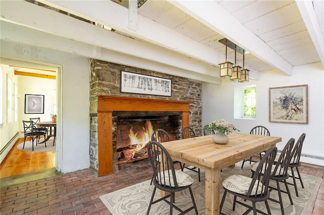 dining space with beam ceiling and a stone fireplace