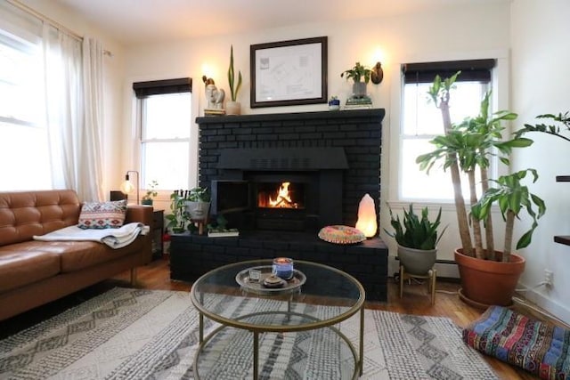 sitting room featuring baseboard heating, a brick fireplace, a wealth of natural light, and hardwood / wood-style flooring