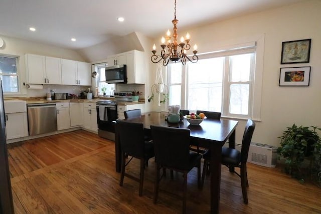 dining area featuring vaulted ceiling, dark hardwood / wood-style flooring, a wall mounted air conditioner, and a notable chandelier