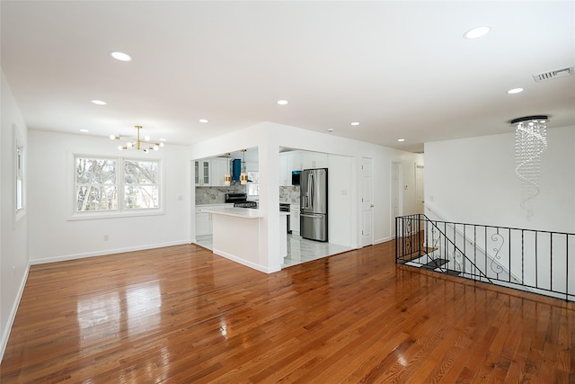 unfurnished living room with an inviting chandelier and light hardwood / wood-style floors