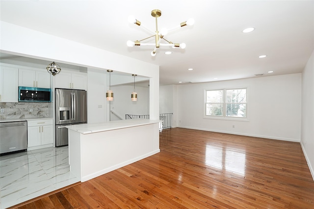 kitchen with appliances with stainless steel finishes, decorative light fixtures, white cabinetry, tasteful backsplash, and a chandelier