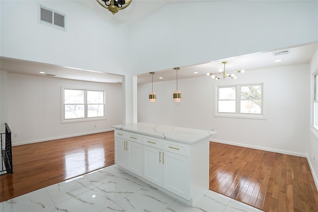 kitchen featuring decorative light fixtures, light hardwood / wood-style floors, an inviting chandelier, white cabinetry, and light stone counters