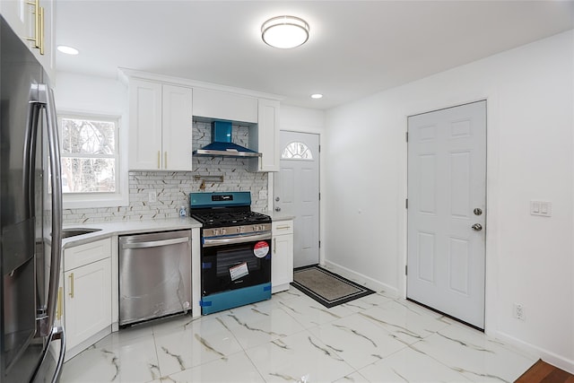 kitchen featuring white cabinetry, appliances with stainless steel finishes, wall chimney exhaust hood, and tasteful backsplash