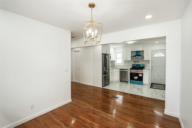 kitchen featuring wall chimney range hood, decorative backsplash, white cabinetry, hanging light fixtures, and stainless steel appliances