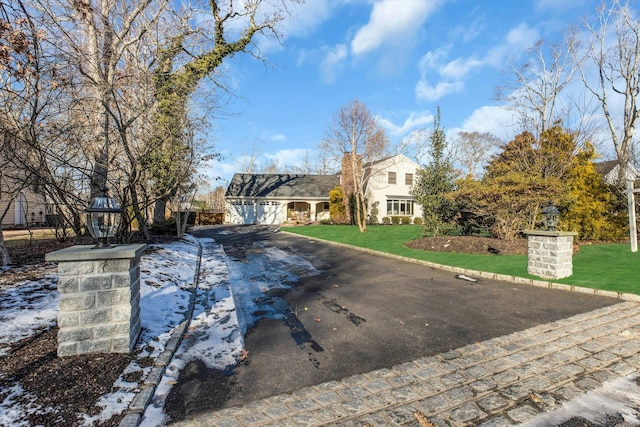 view of front facade featuring aphalt driveway, an attached garage, a chimney, and a front lawn