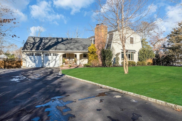 view of front of property featuring a chimney, a porch, a garage, driveway, and a front lawn