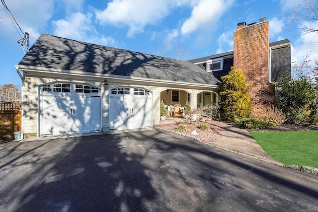 view of front of home featuring a garage, a chimney, aphalt driveway, and roof with shingles