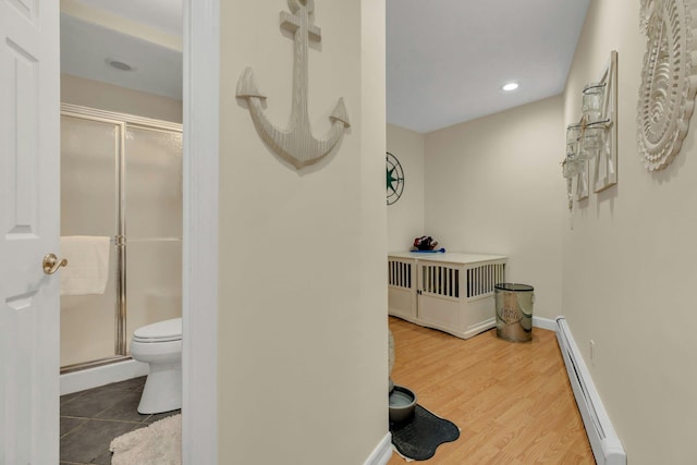 full bathroom featuring baseboards, toilet, wood finished floors, a shower stall, and a baseboard heating unit