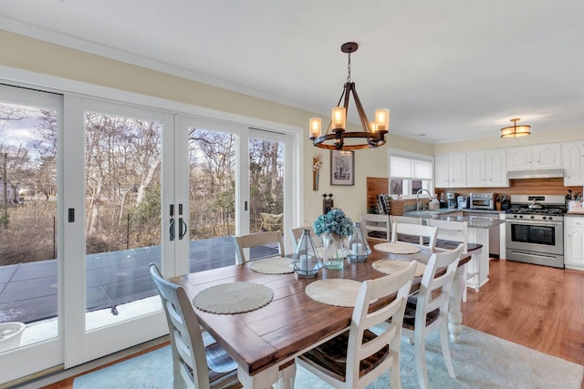 dining space with french doors, a toaster, crown molding, light wood-style flooring, and a chandelier