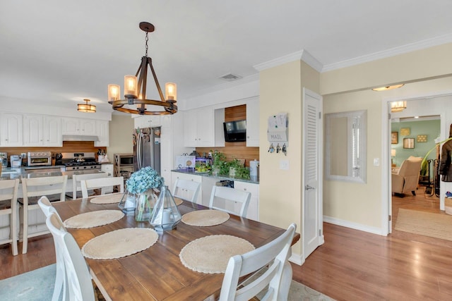 dining room featuring visible vents, light wood-style floors, baseboards, an inviting chandelier, and crown molding