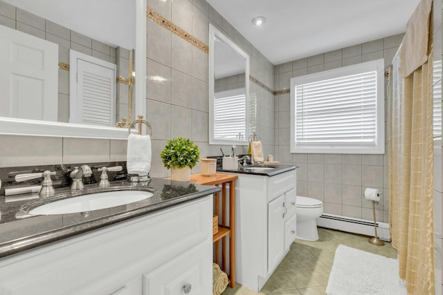 full bath featuring tile walls, two vanities, tile patterned floors, baseboard heating, and a sink