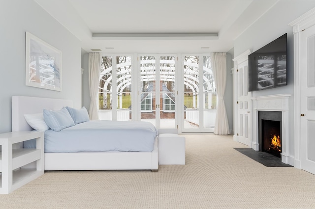 bedroom with access to outside, light colored carpet, and a tray ceiling