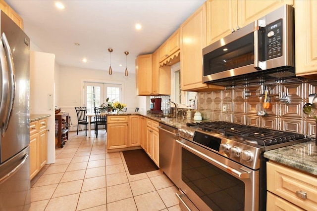 kitchen with light tile patterned floors, stainless steel appliances, light brown cabinetry, and dark stone countertops