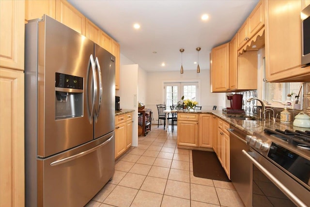 kitchen with kitchen peninsula, appliances with stainless steel finishes, light brown cabinets, and dark stone counters