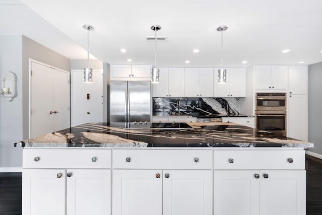 kitchen with appliances with stainless steel finishes, white cabinetry, backsplash, dark stone counters, and hanging light fixtures