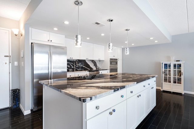 kitchen featuring appliances with stainless steel finishes, tasteful backsplash, white cabinets, a kitchen island, and dark stone counters