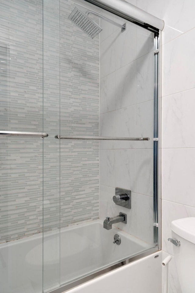 bathroom featuring toilet and combined bath / shower with glass door