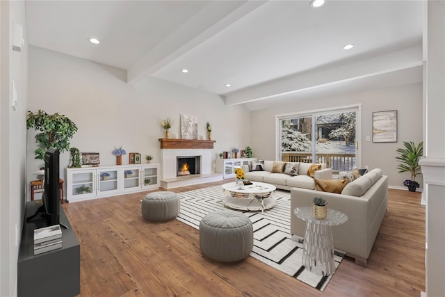 living area featuring lofted ceiling with beams, a lit fireplace, wood finished floors, and recessed lighting