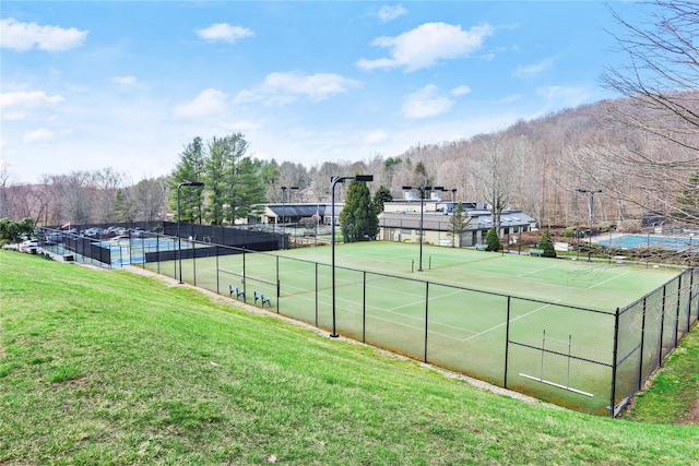 view of tennis court with a lawn and fence