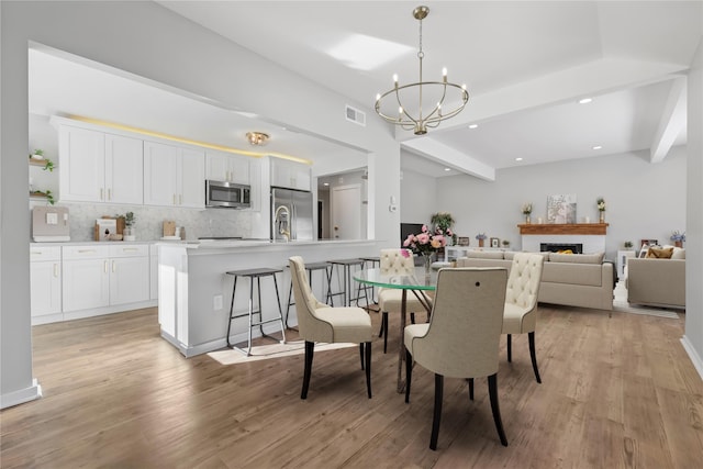 dining area featuring beamed ceiling, light wood finished floors, a chandelier, and visible vents