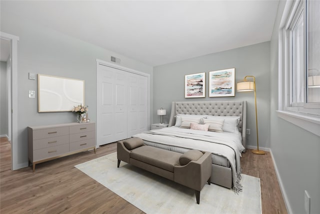 bedroom with visible vents, baseboards, wood finished floors, and a closet