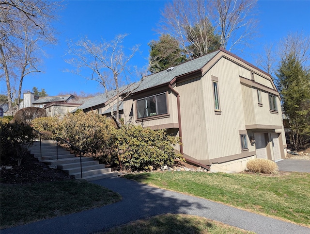 view of side of home with a garage, driveway, stairway, and a shingled roof