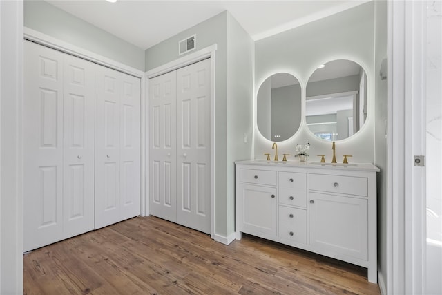 bathroom with visible vents, double vanity, a closet, wood finished floors, and a sink
