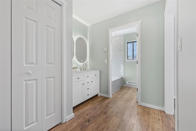 full bath featuring vanity, wood finished floors, baseboards, a bathtub, and a baseboard radiator