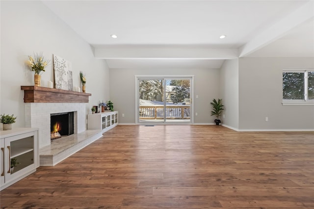 unfurnished living room with a brick fireplace, beamed ceiling, baseboards, and wood finished floors