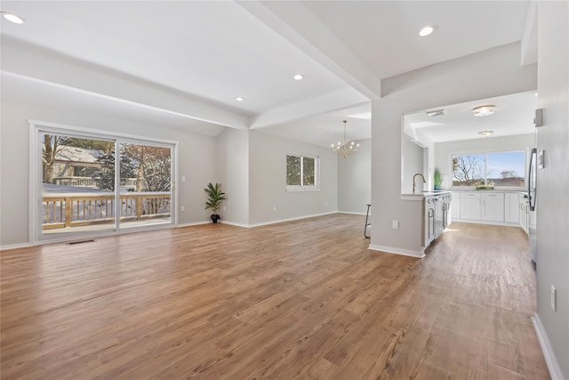 unfurnished living room featuring an inviting chandelier, baseboards, light wood-style flooring, and beam ceiling