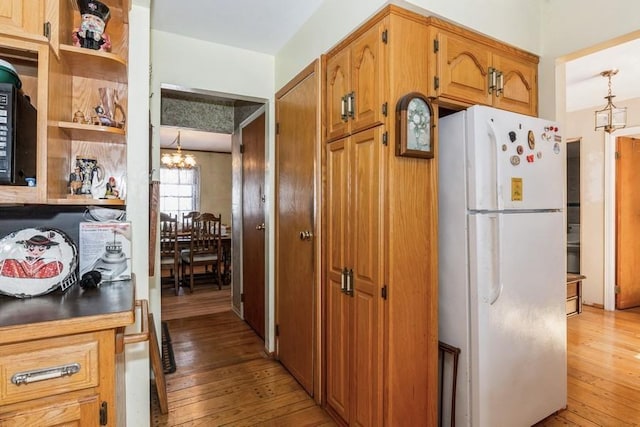 kitchen featuring light wood-type flooring, an inviting chandelier, and white fridge